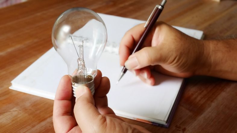 une personne tient une ampoule dans sa main et écrit de l'autre