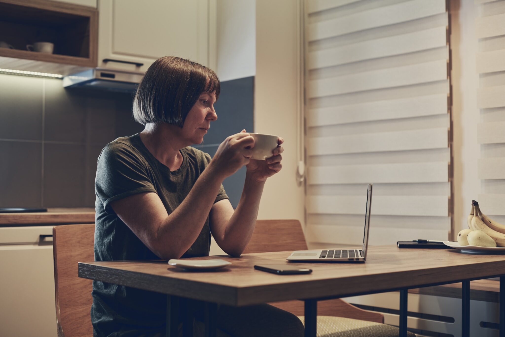 une femme boit un café tout en regardant l'écran de son ordinateur