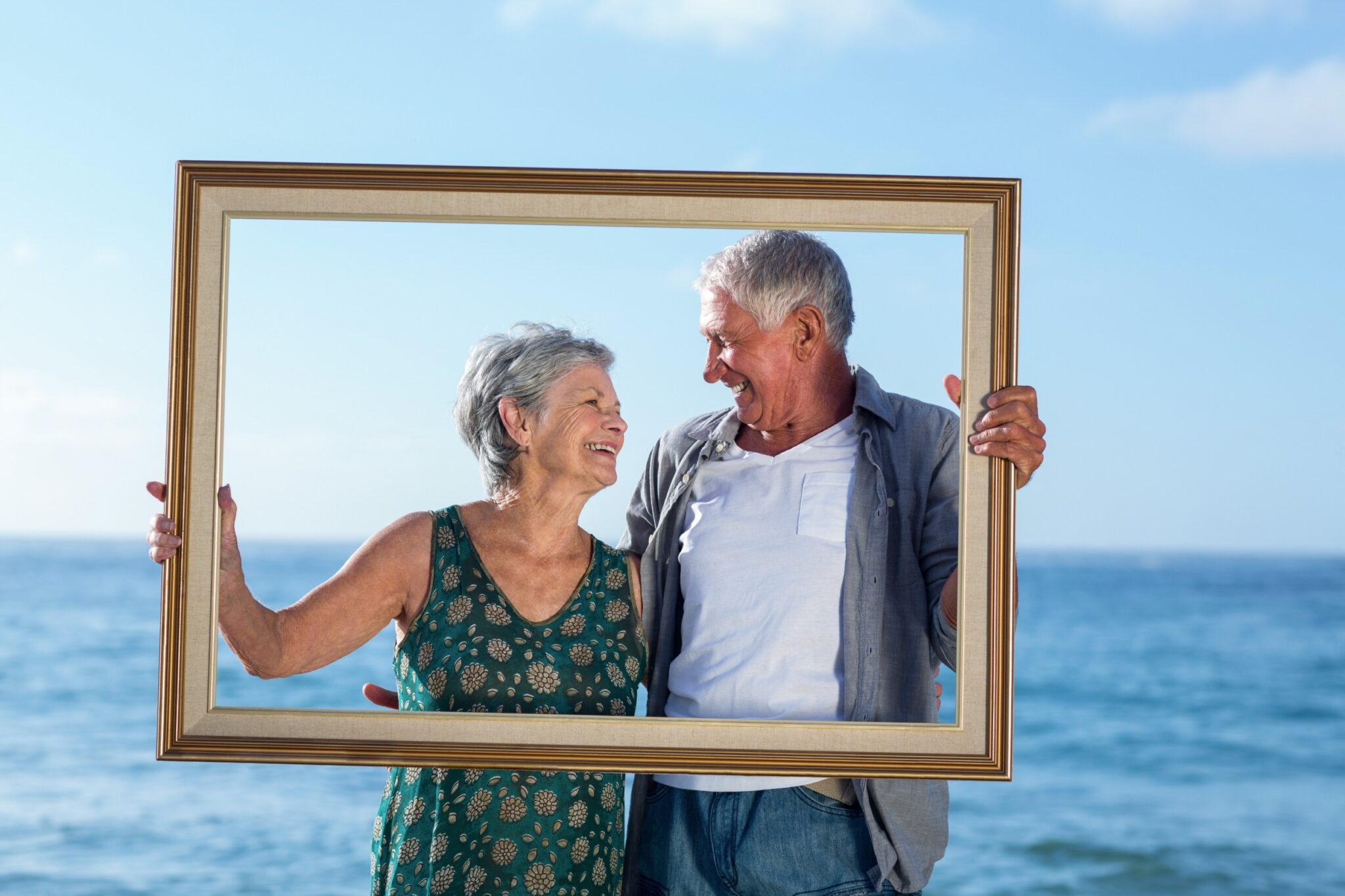 un couple de retraités se regardent et se sourient, dos à la mer