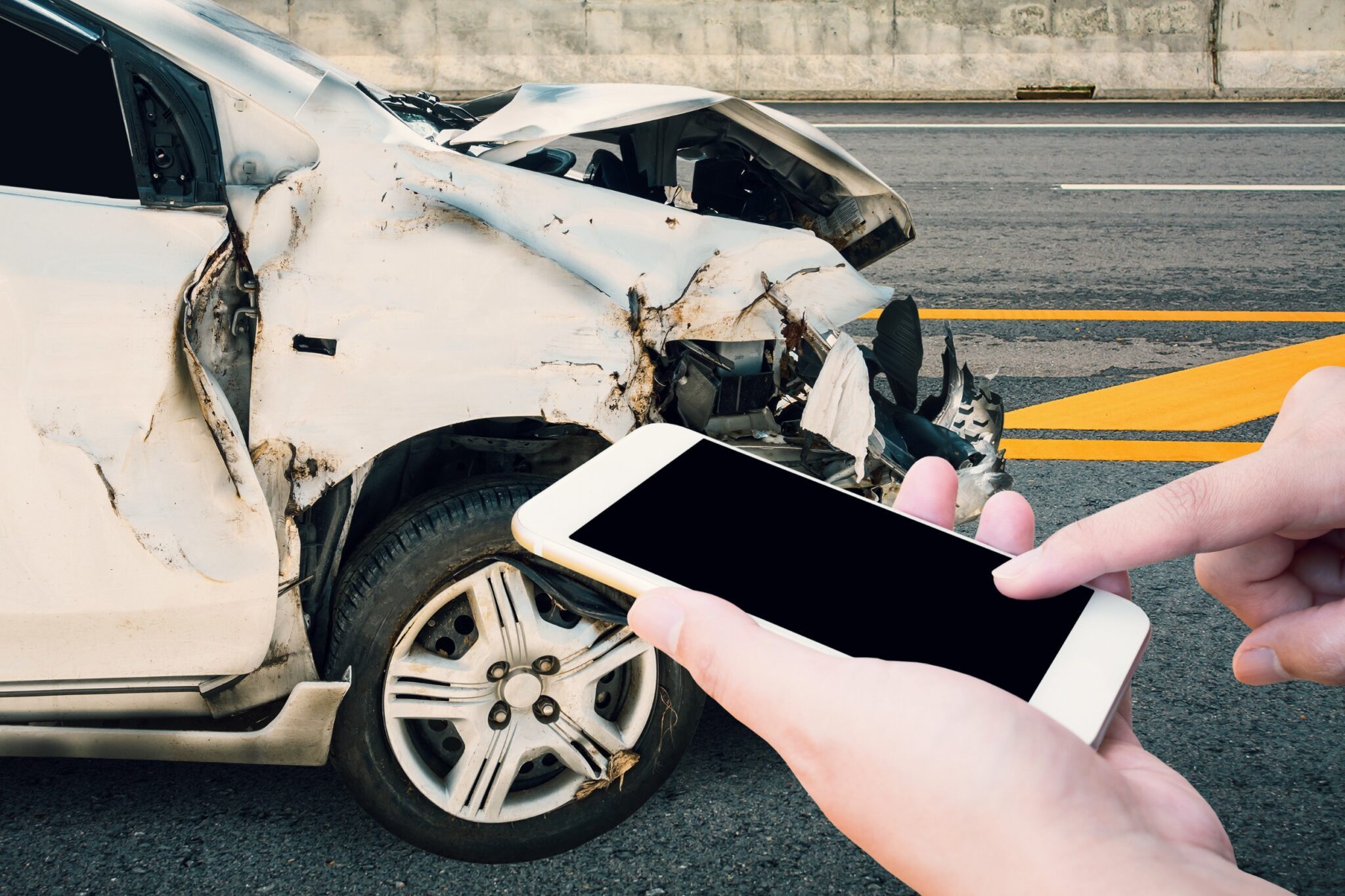 devant une voiture accidentée, des mains tiennent un smartphone 