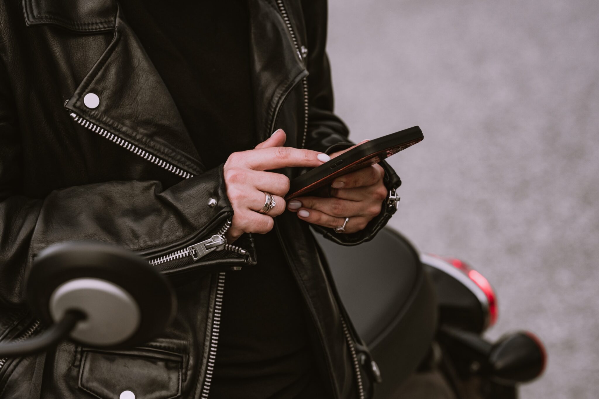 une femme est assise sur son scooter, à l'arrêt et consulte sur téléphone