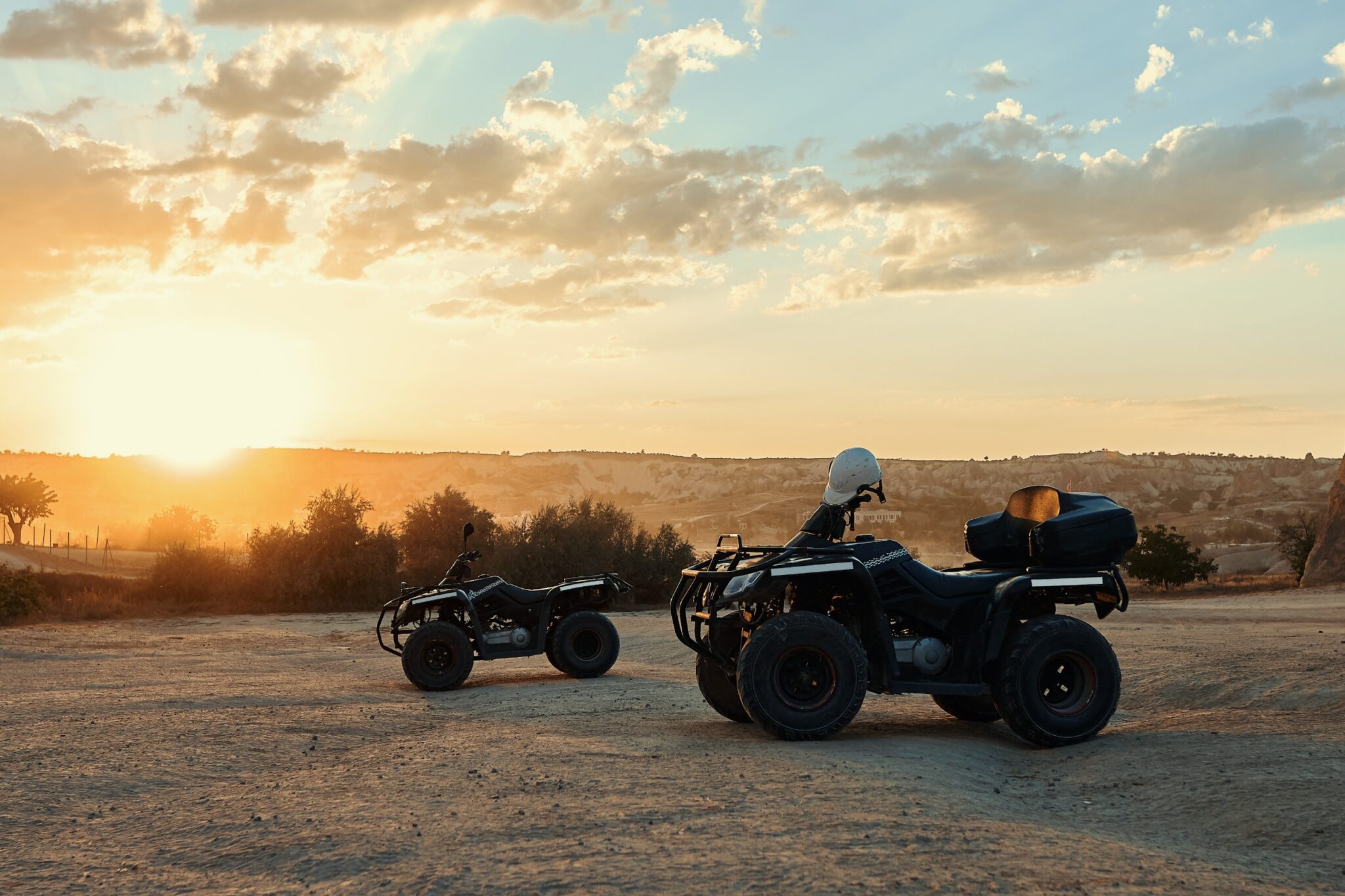 deux quads stationnent sur un terrain, avec en fond un coucher de soleil