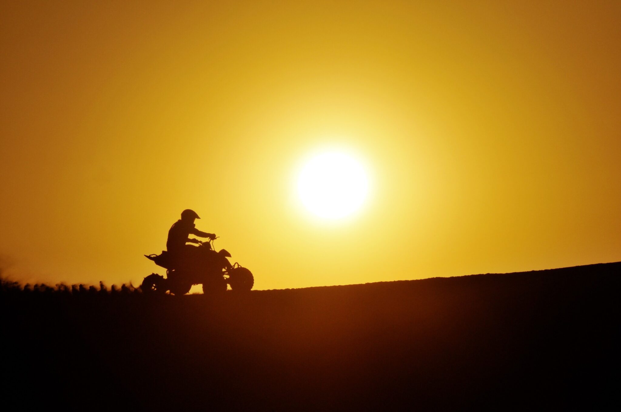 un personne conduit un quad sur une colline avec un coucher de soleil en fond