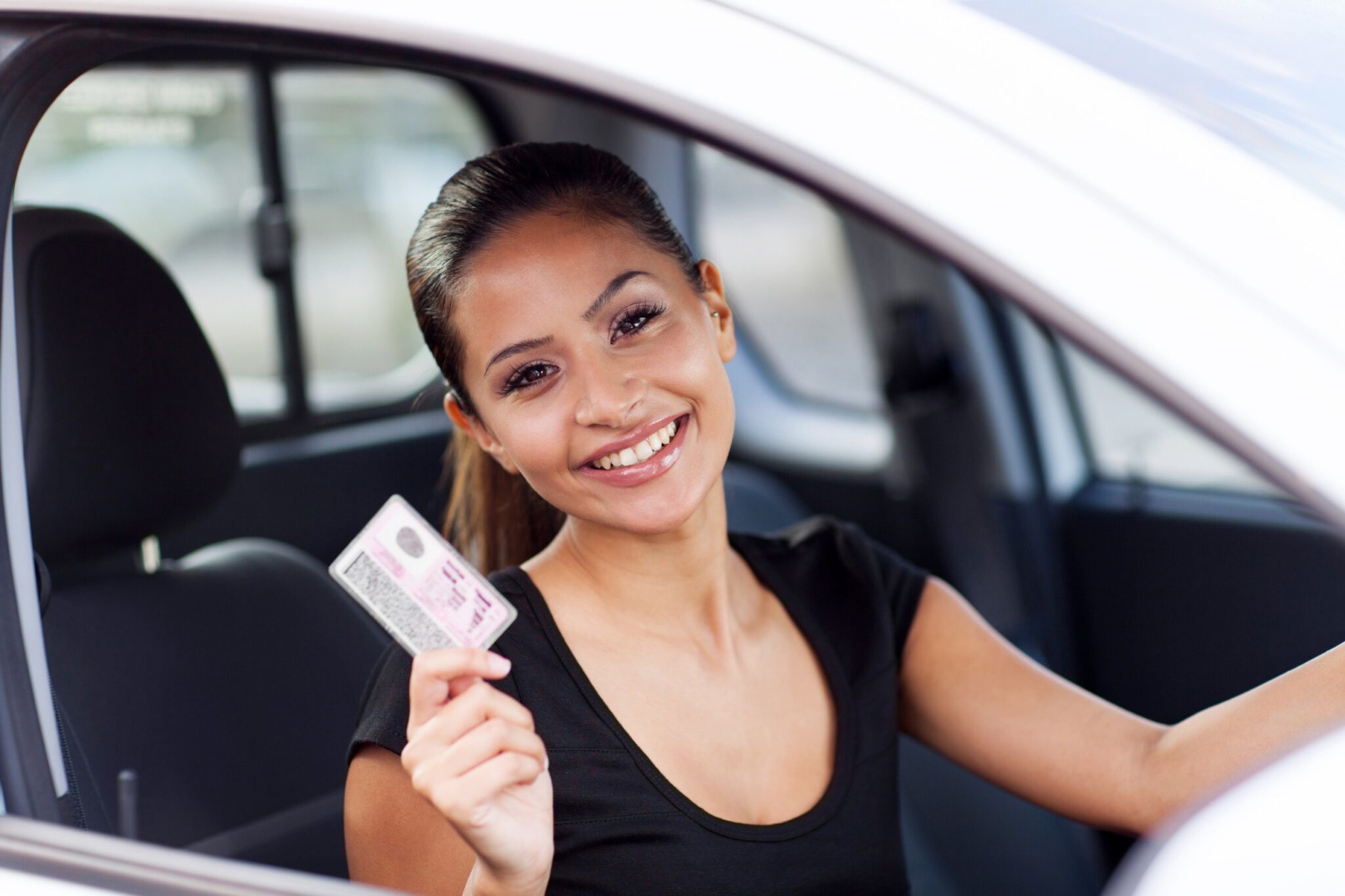 une jeune femme sourit et tient son permis de conduire dans la main