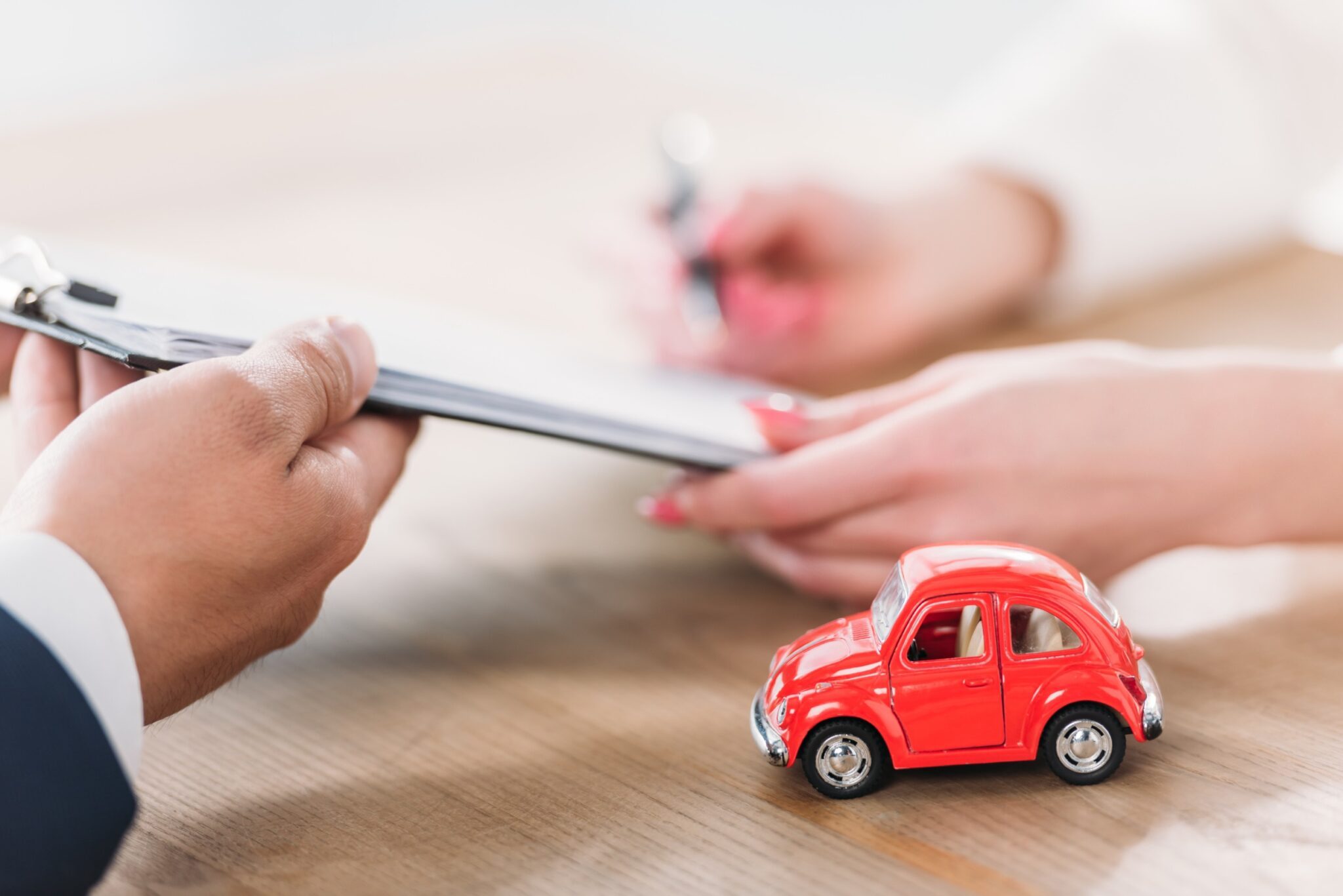 gros plan sur les mains d'une femme signant un contrat avec une petite voiture rouge près de sa main