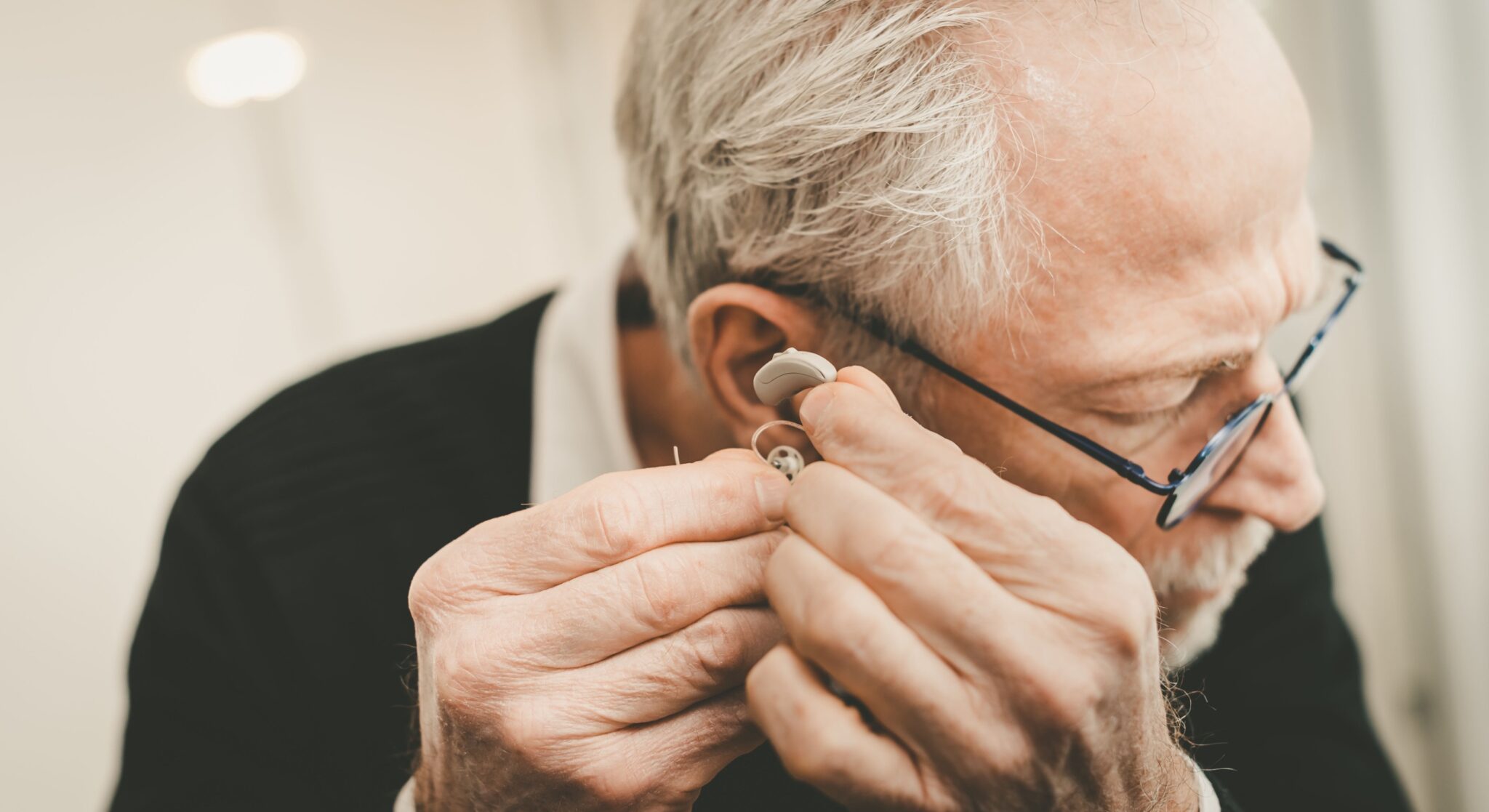 un homme aux cheveux blancs met sa prothèse auditive