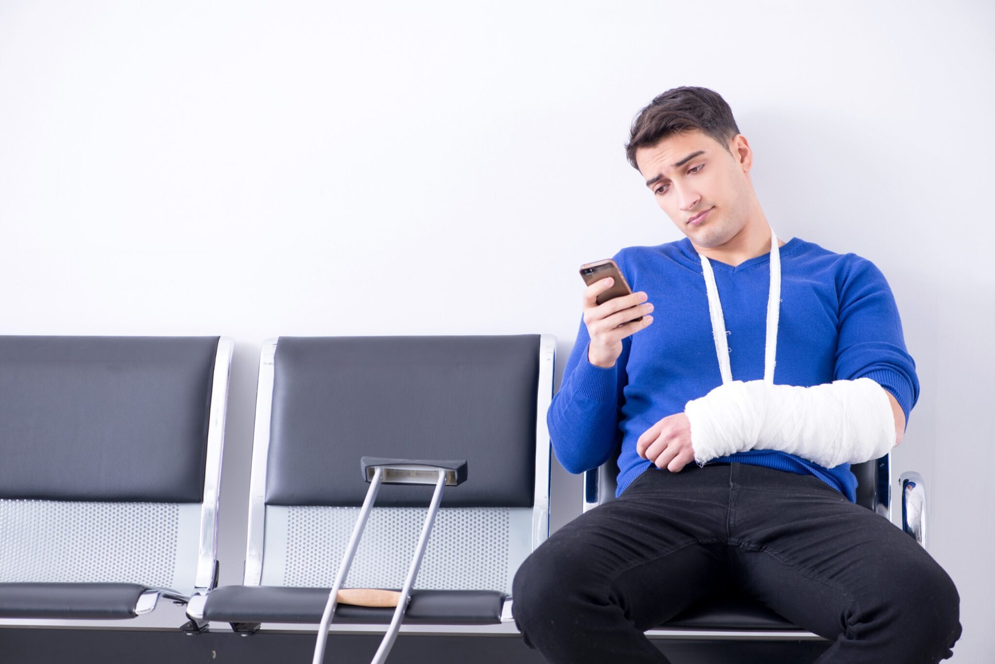 un jeune homme, avec un plâtre, attend dans une salle d'attente, consultant son téléphone