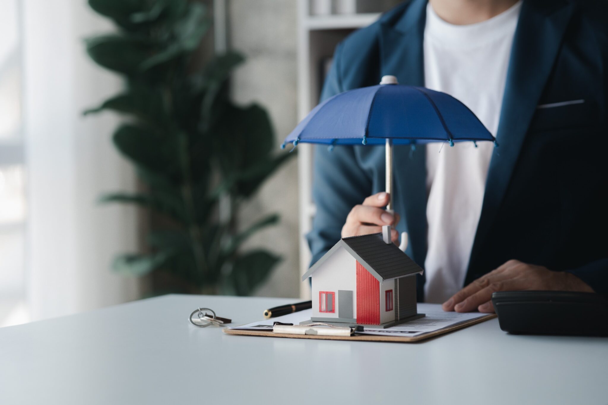 un homme tient un parapluie miniature au dessus de la maquette d'une maison