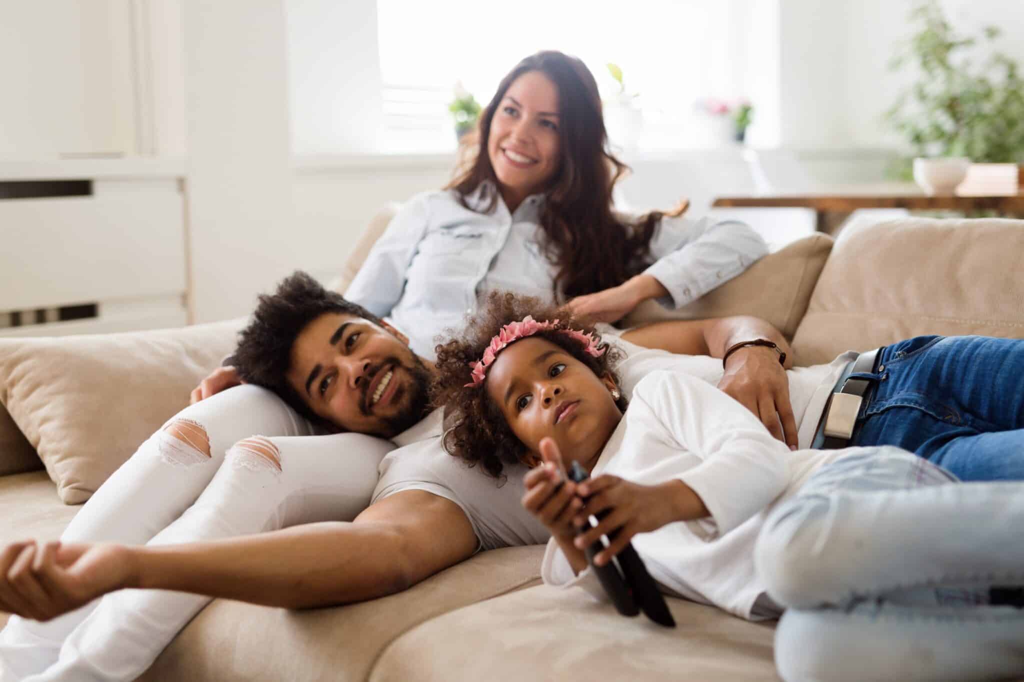 une famille est sur son canapé, en train de regarder la télé