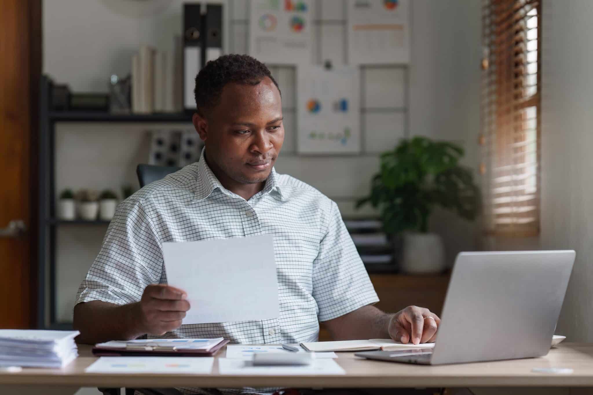 Un homme devant son PC avec un document à la main