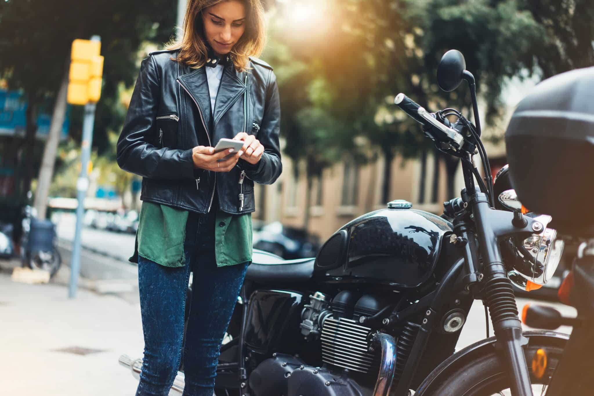 Une femme qui regarde son téléphone à côté de sa moto garée
