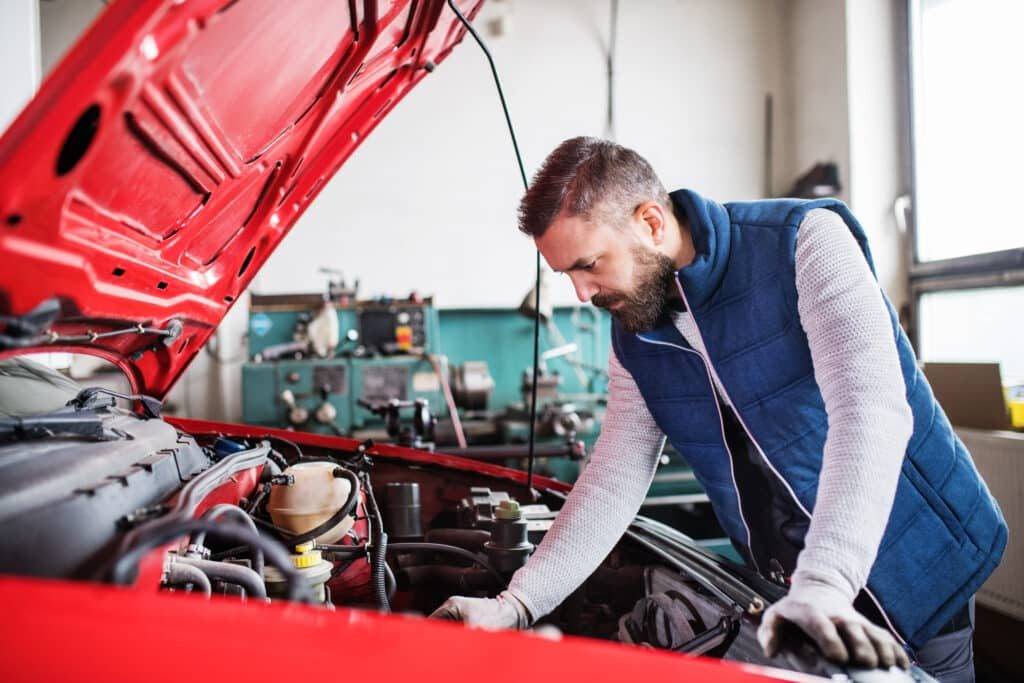 homme regardant sous le capot d'une voiture rouge