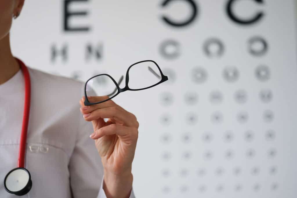 Femme ophtalmologue réalise un test de vue à son patient et tient des lunettes dans une main