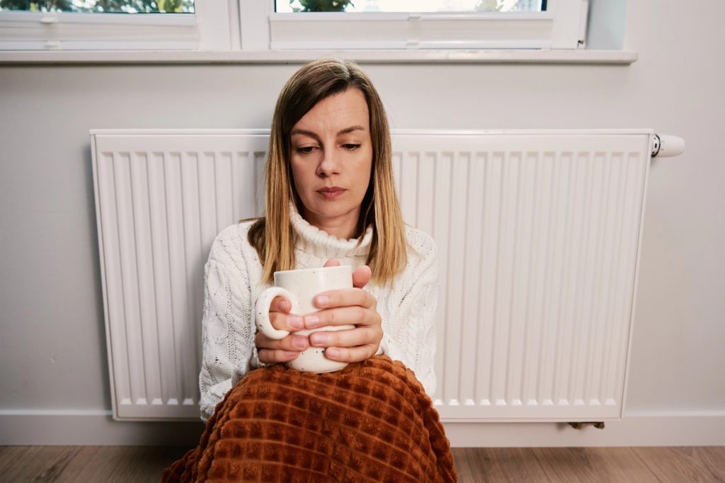 une femme préoccupée assise sur son radiateur